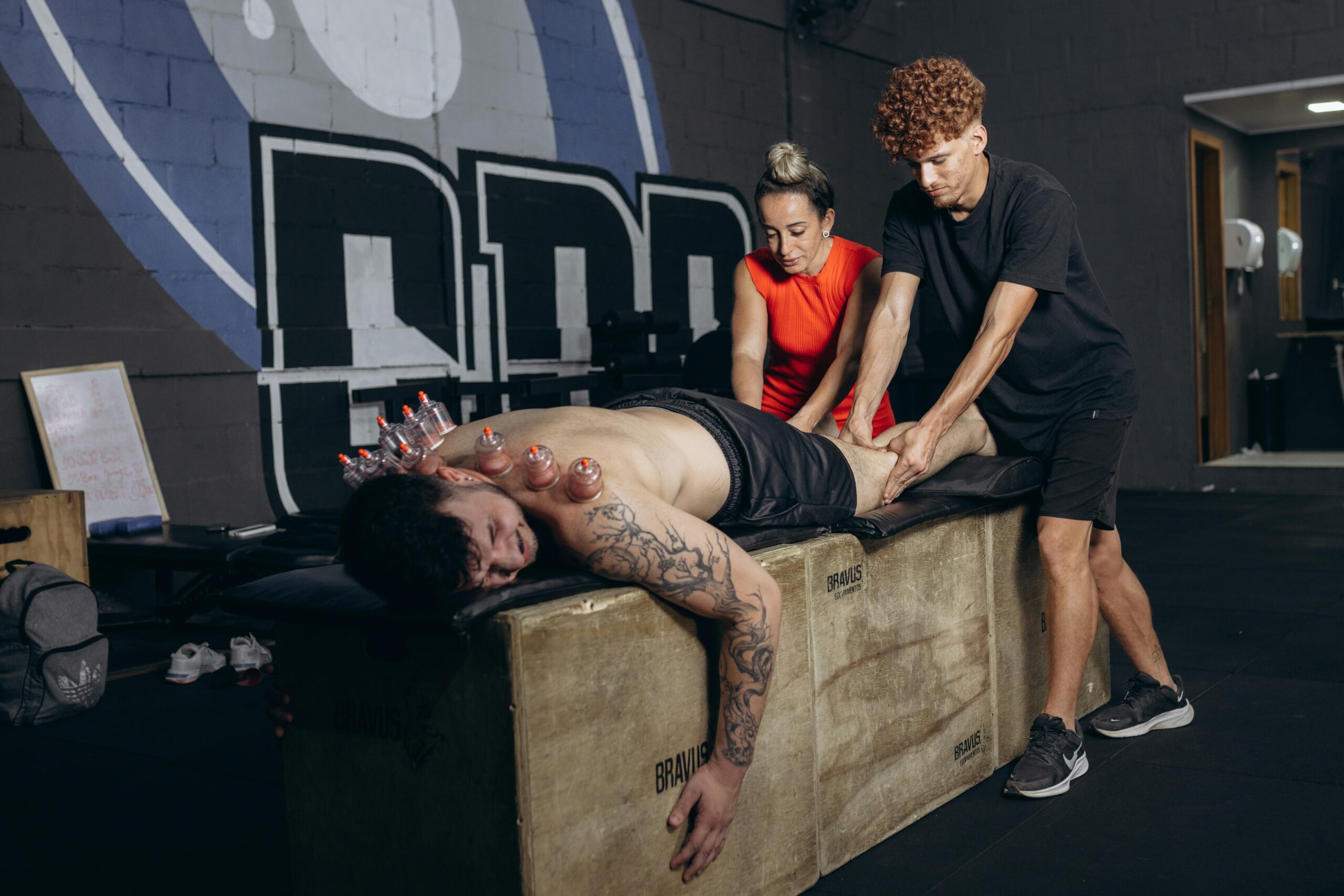 Athlete receives cupping therapy and massage for recovery in a gym setting.