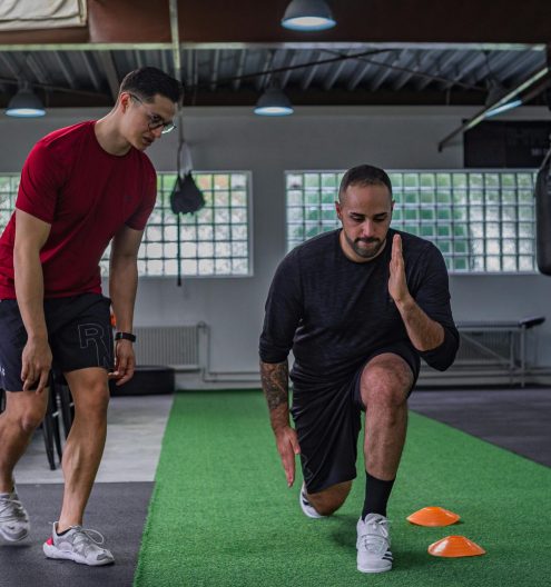 Full body of focused man in sportswear doing stretching exercises with coach in contemporary fitness center